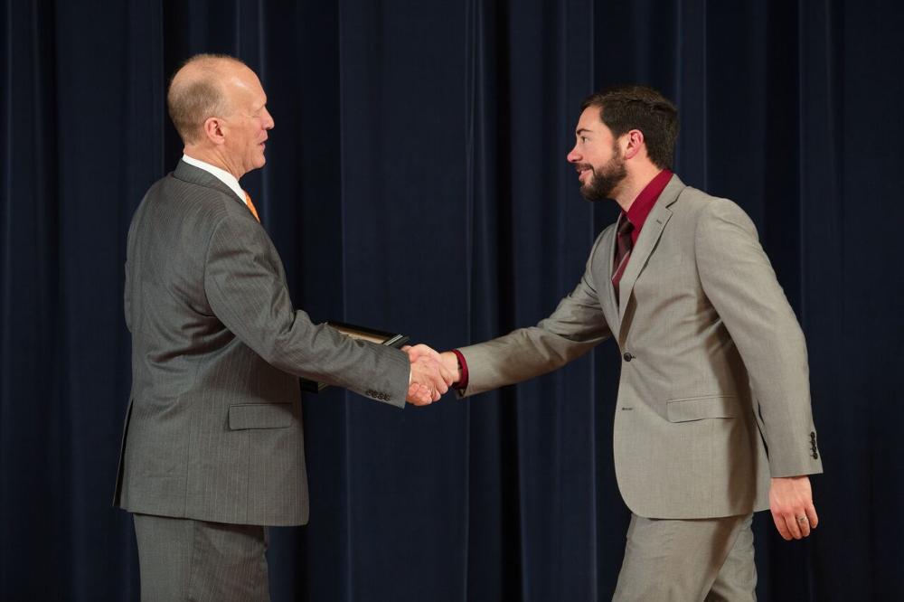 Doctor Potteiger shaking hands with an award recipient in a light grey suit and a red shirt